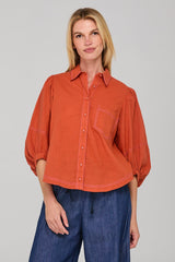Woman wearing an orange shirt and blue jeans against a gray background