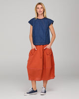 Woman wearing a dark blue denim top and orange skirt on a gray background
