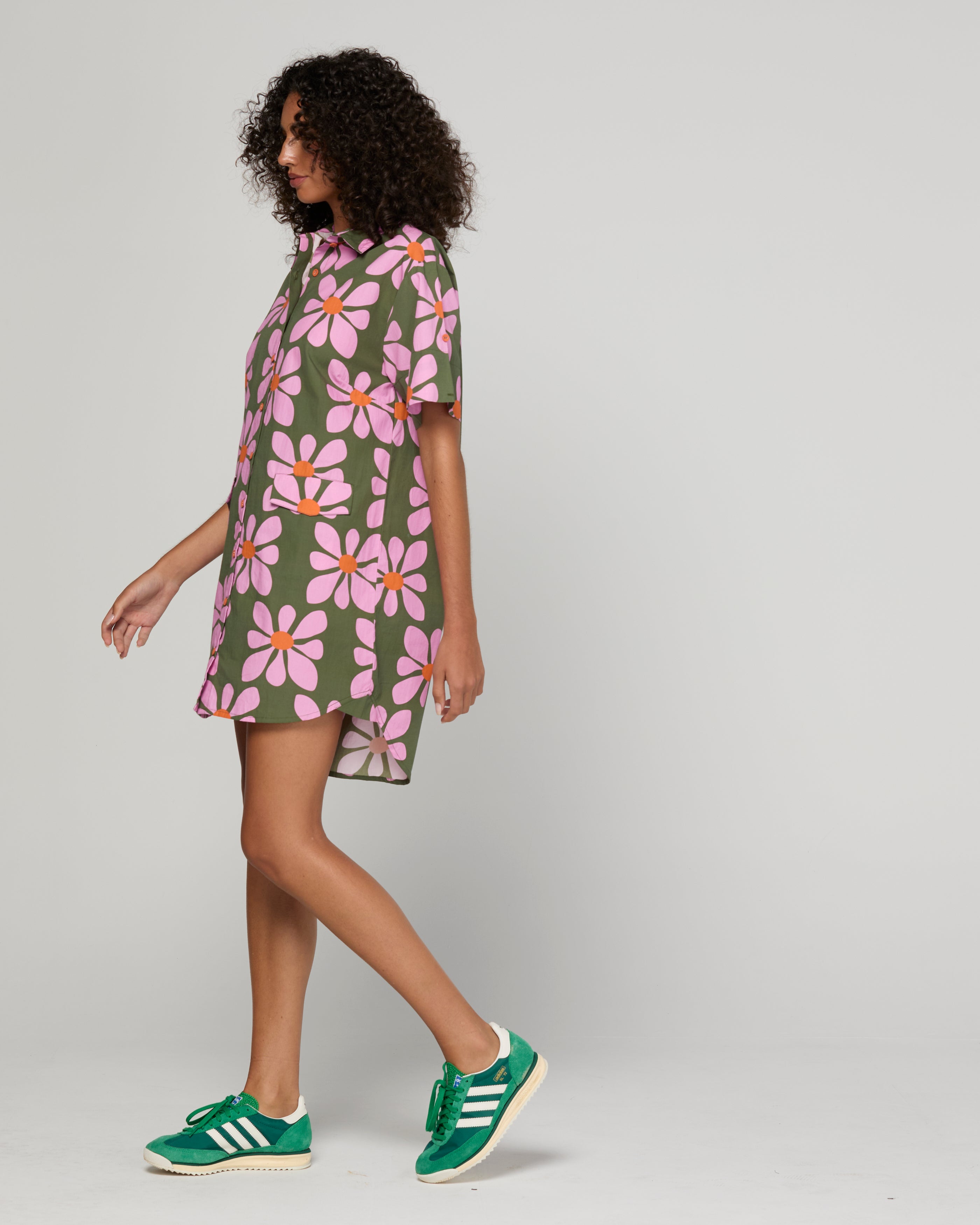 Woman wearing a floral dress with green sneakers on a plain background