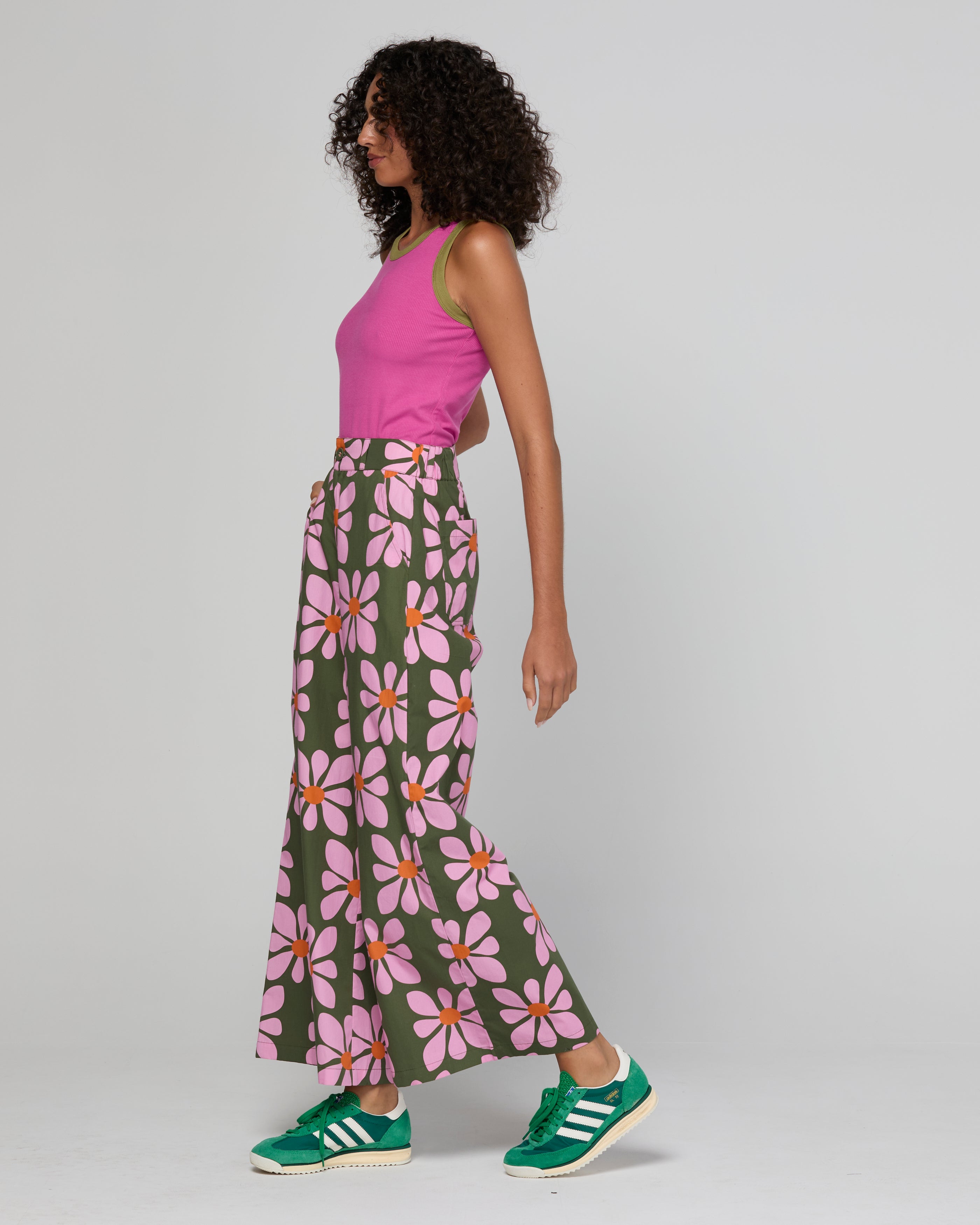 Woman wearing a pink top and floral pants with green sneakers on a plain background