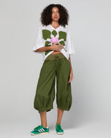 Woman wearing a white shirt with a floral design and green pants on a plain background