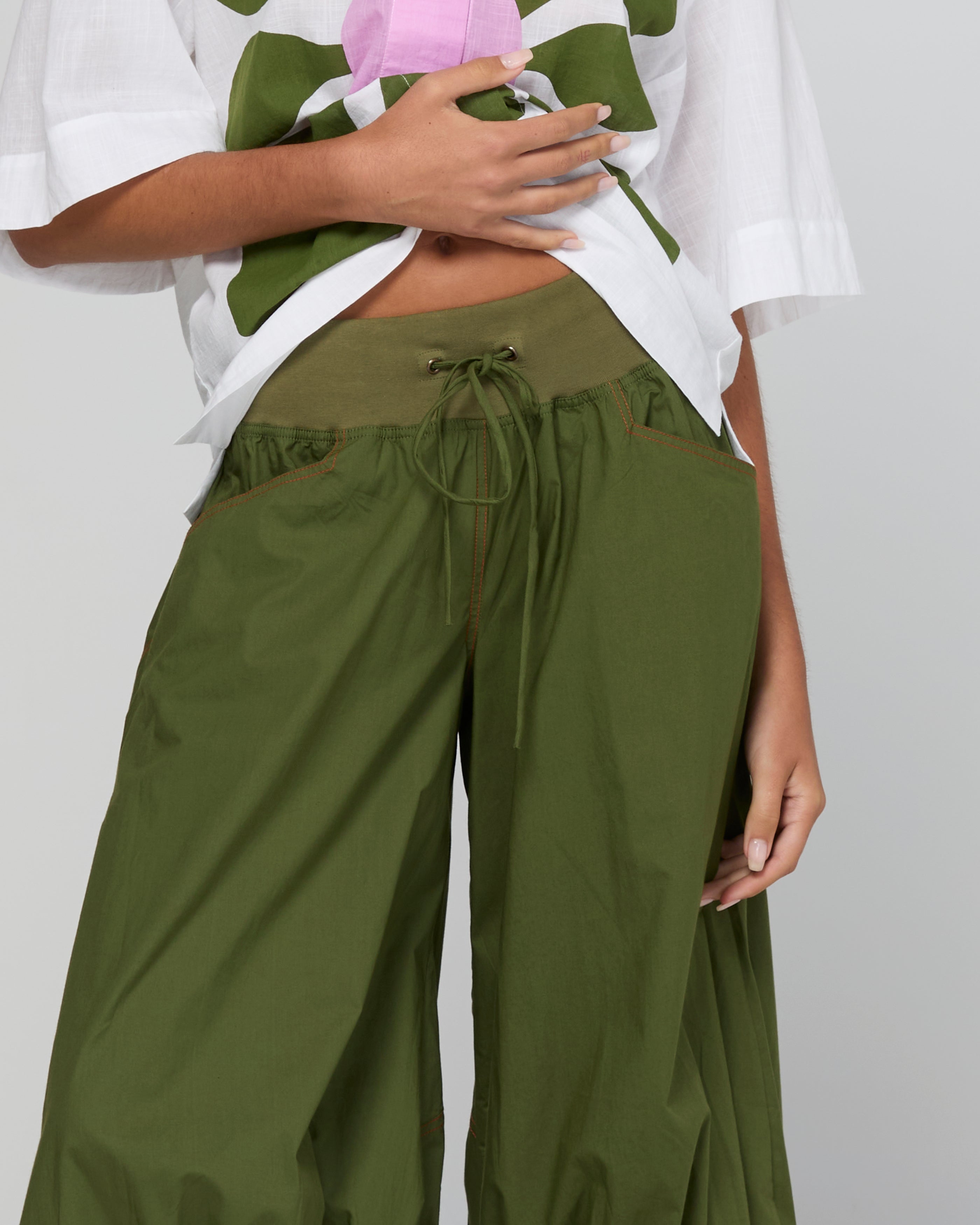Person wearing green wide-leg pants and a white top with a floral pattern on a light gray background