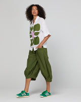 Woman wearing a white shirt with a green floral pattern and green pants on a plain background