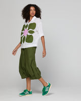 Woman wearing a white shirt with a green floral design, green pants, and green sneakers on a light gray background