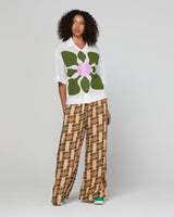 Woman wearing a white shirt with a large green flower design and patterned pants