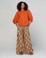 Woman wearing an orange blouse and patterned pants on a white background