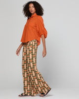 Woman wearing an orange top and patterned pants on a plain background