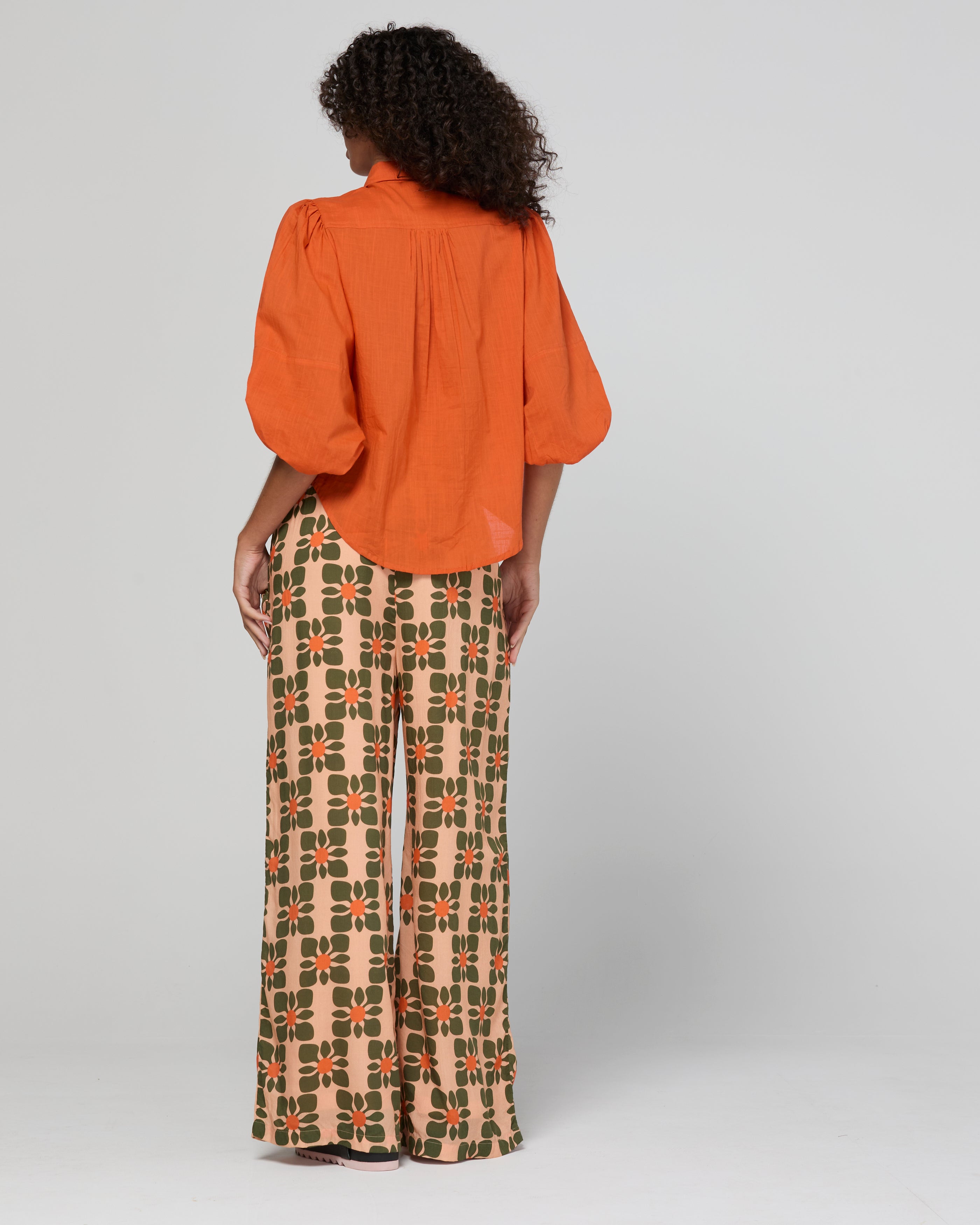 Person wearing an orange blouse and patterned pants on a plain background