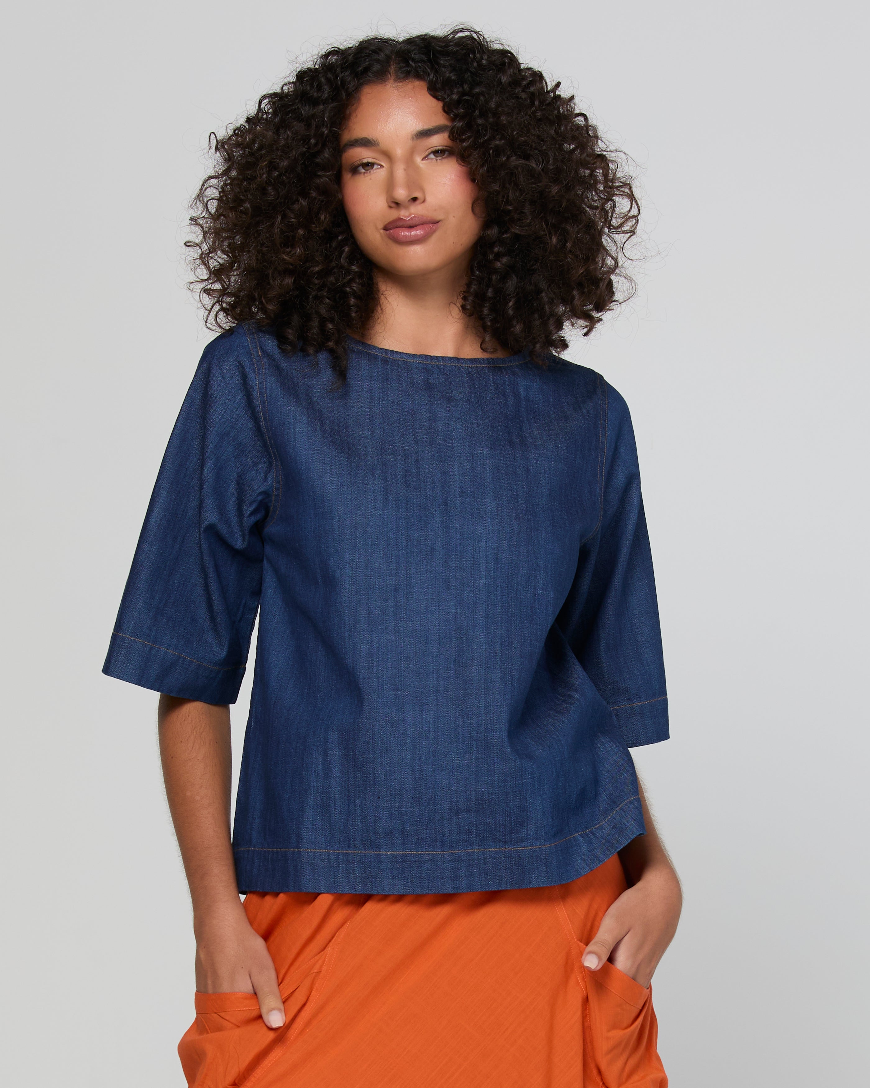 Woman wearing a blue denim top and orange pants on a plain background