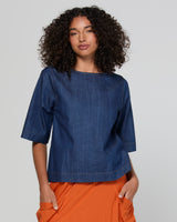 Woman wearing a blue denim top and orange pants on a plain background