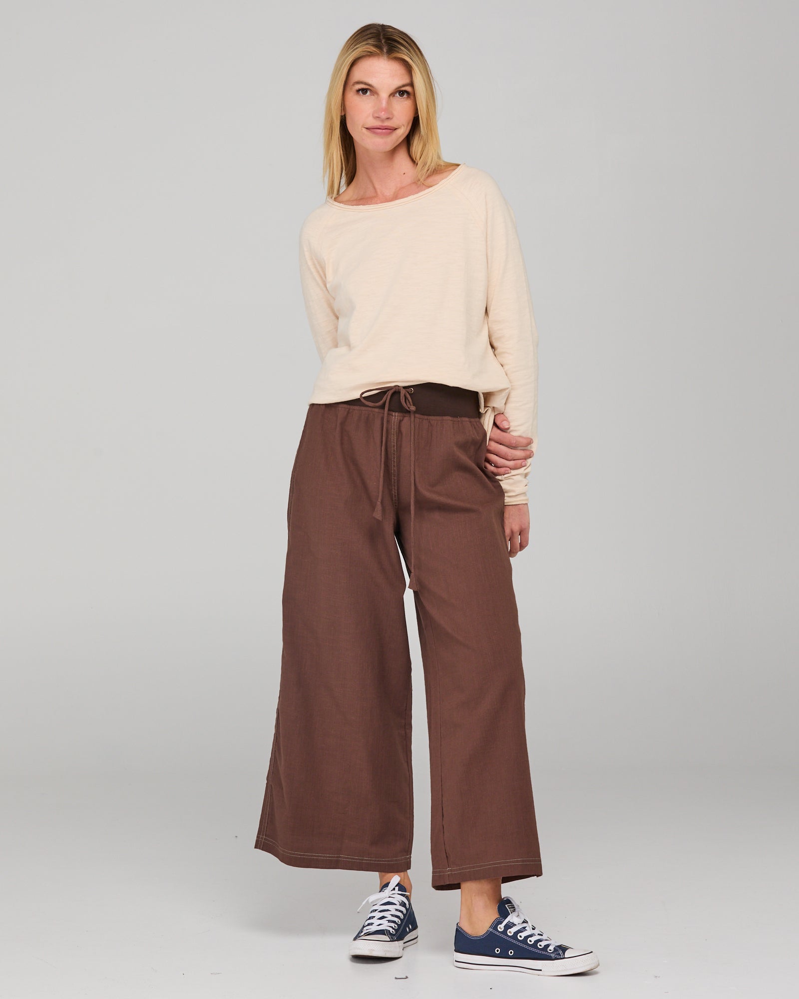 Woman wearing a cream top and brown wide-leg pants on a plain background