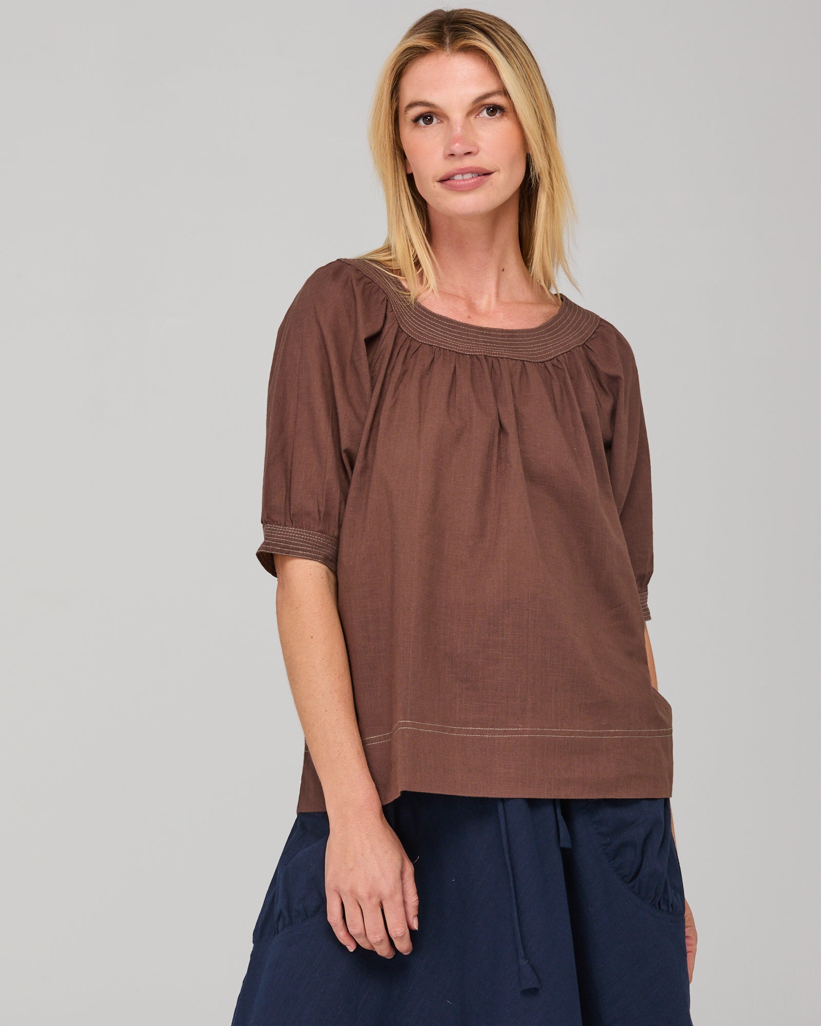 Woman wearing a brown round neck blouse with a plain background