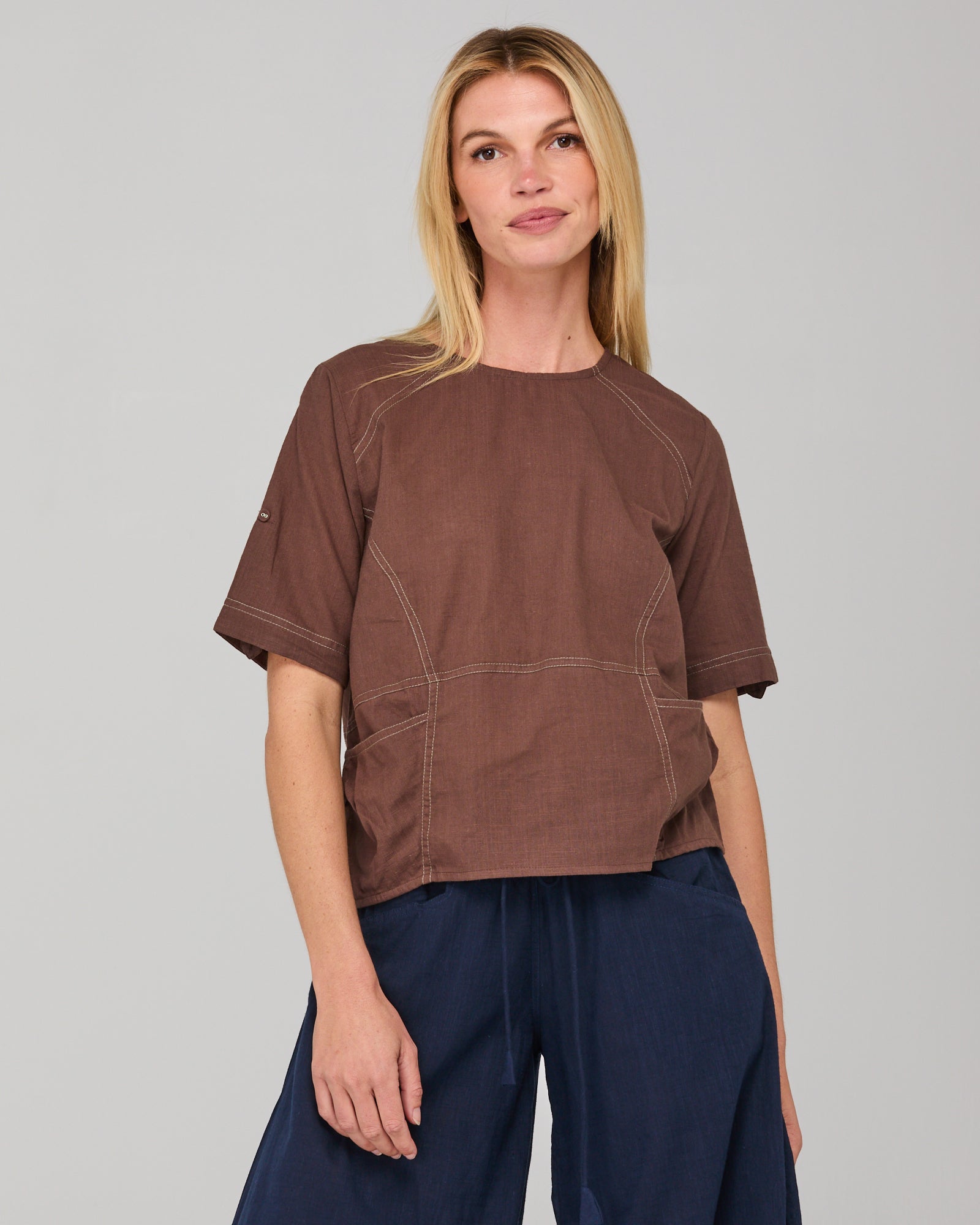 Woman wearing a brown top with stitching design on a gray background