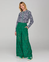 Woman wearing a patterned top and green lace pants on a white background