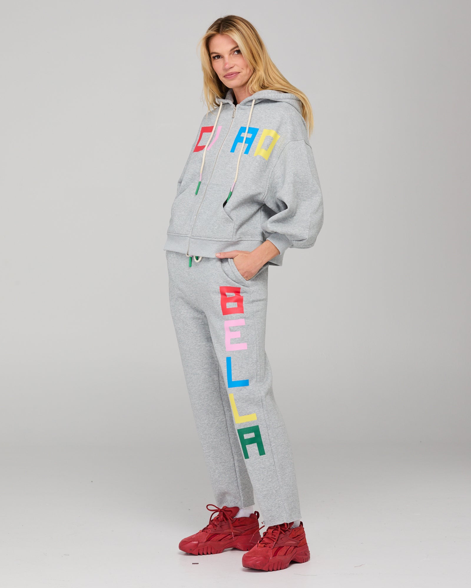 Person wearing a gray tracksuit set with colorful letters on a plain background