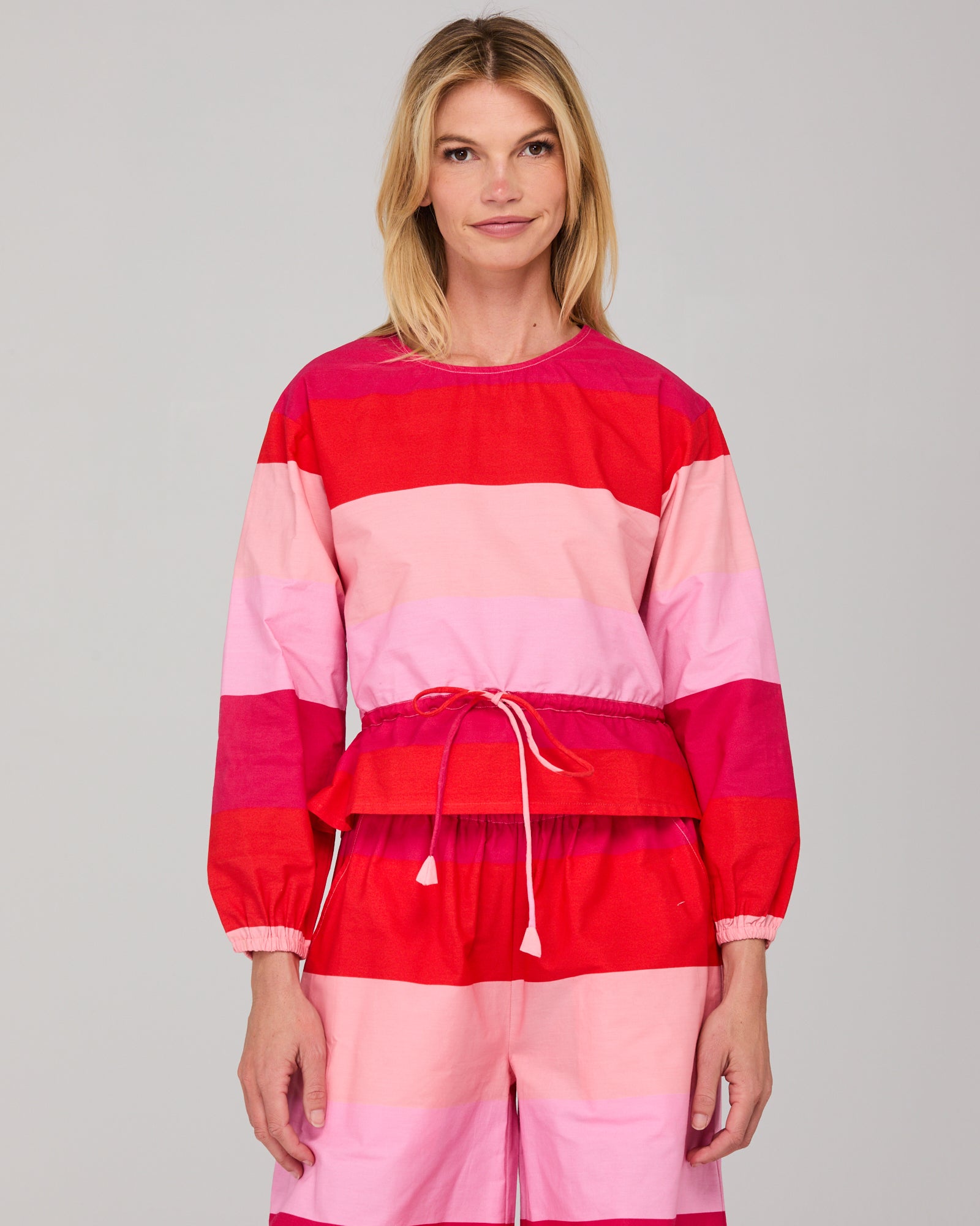Woman wearing a red and pink striped long sleeved top on a gray background