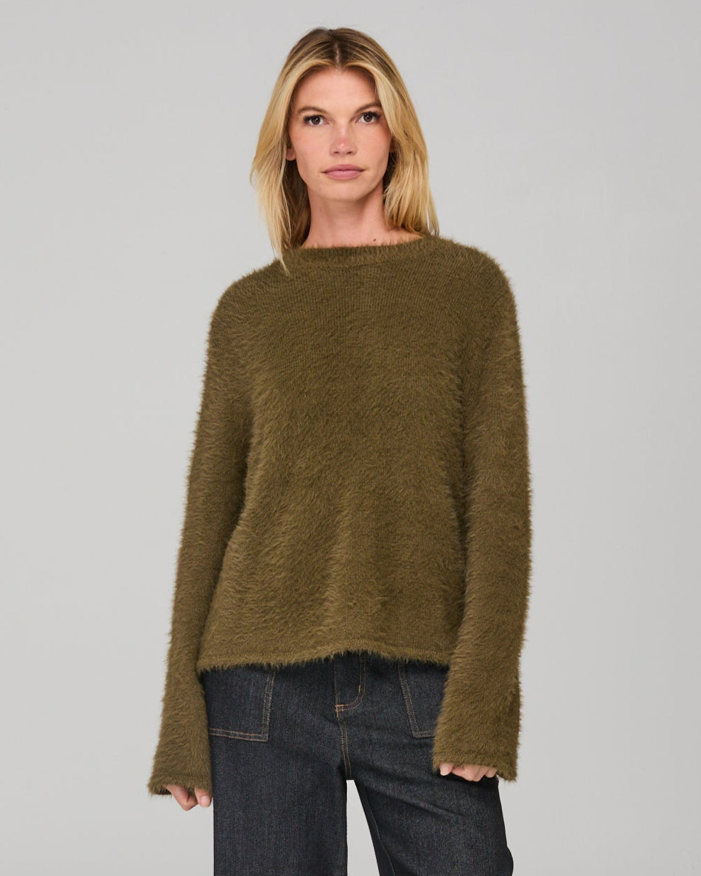 Woman wearing a khaki green sweater and dark denim jeans on a gray background