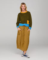 Woman wearing a khaki sweater with blue trim and a mustard checkered skirt on a grey background