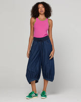 Woman wearing a pink tank top and denim balloon pants on a white background