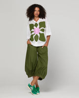 Person wearing a white shirt with a large green flower design and green pants on a plain background