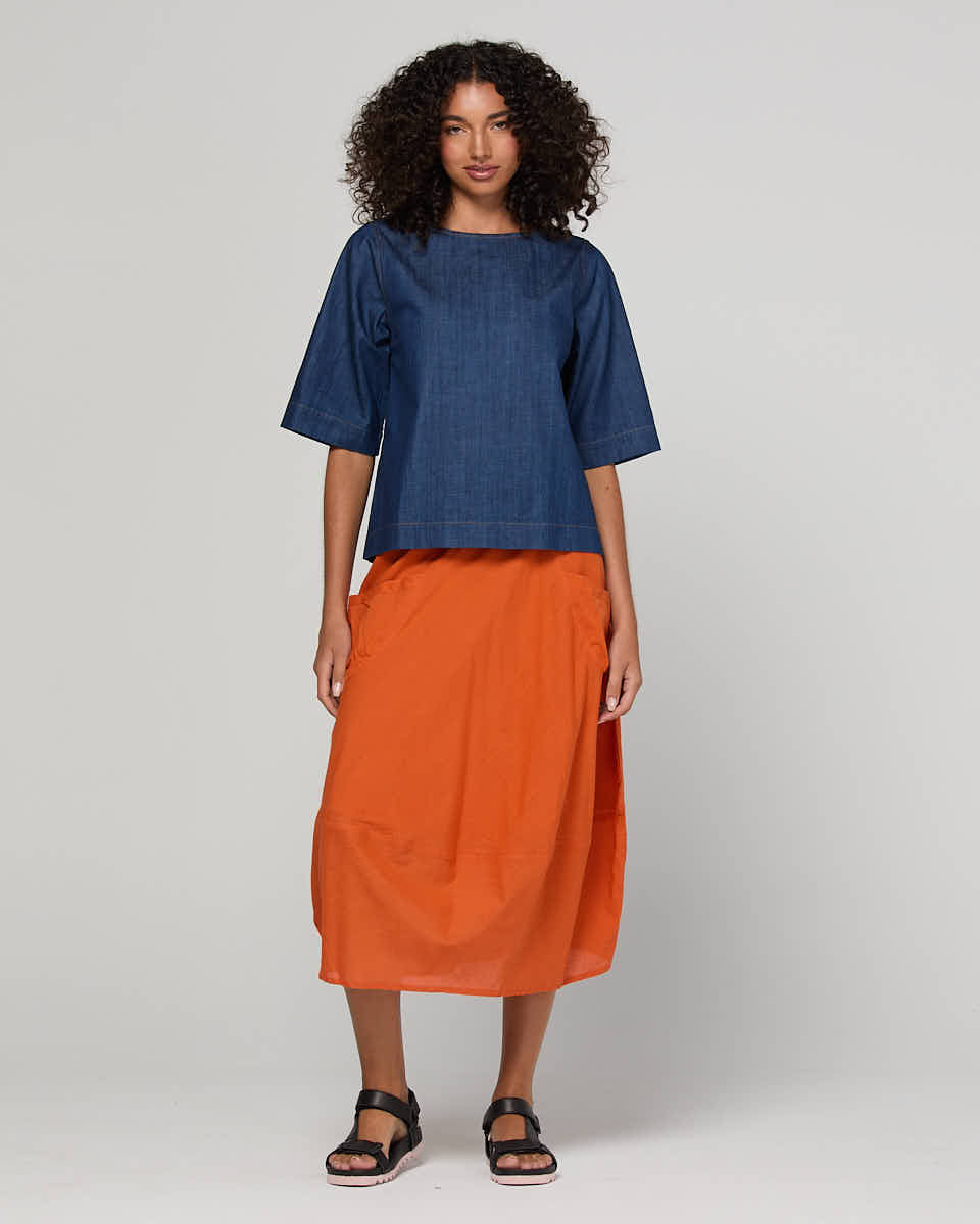 Woman wearing a blue top and orange skirt on a white background
