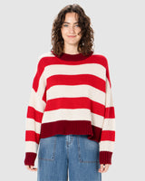 A woman wearing a red and white horizontally striped knit sweater with a crew neck and blue jeans.